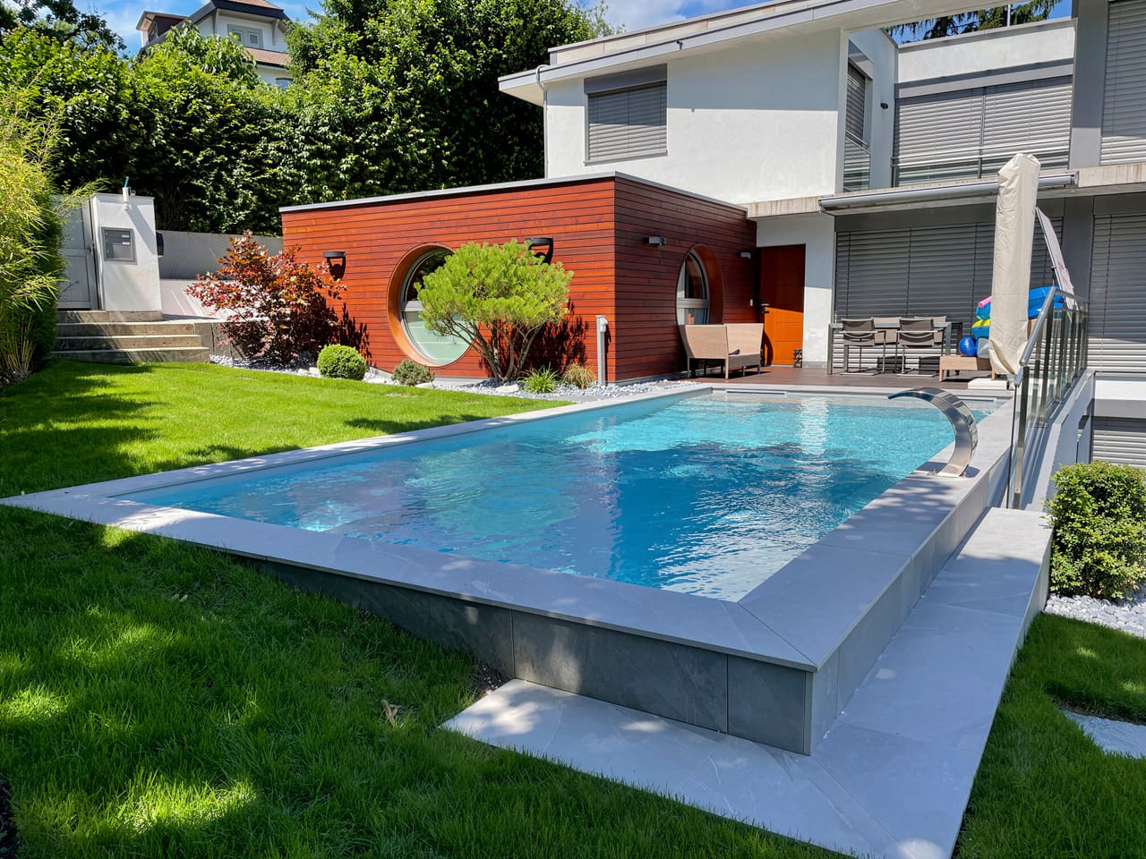 Piscine traditionnelle à la ligne contemporaine dans un jardin arboré
